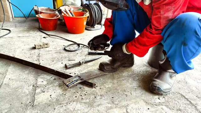 Displaying Video A worker wearing protective gear is welding iron metal with bright sparks in an industrial workshop area. 