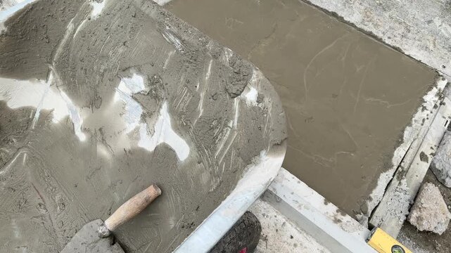Mixing tub with cement mortar next to fresh concrete patch on floor closeup
