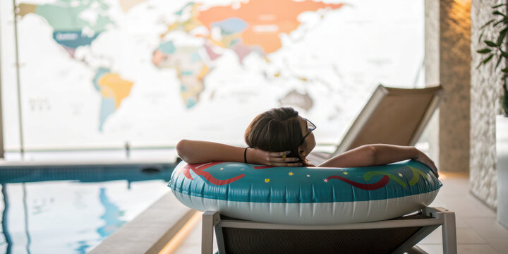Person relaxing on inflatable ring by indoor pool with world map on wall, enjoying calm and peaceful moment
