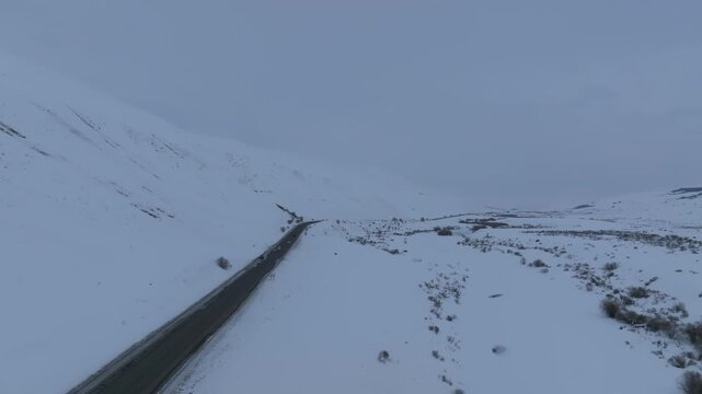 Drone view of a mountain highway crossing Ala-Bel Pass with cars driving through a vast snowy landscape, high-altitude valley and ridges in Kyrgyzstan