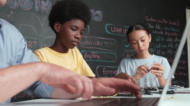 Young student fixing controller while teacher programming engineering code at STEM class. Closeup of instructor hand typing computer while smart girl using electronic tool and blackboard. Edification