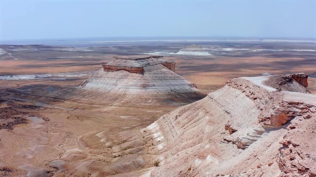 Drone reveals iconic layered mesa formation in Bozzhyra Mangistau Kazakhstan surrounded by vast desert plains, highlighting stratified limestone and chalk textures in remote arid landscape
