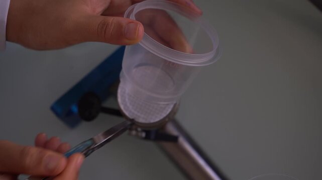 Top-down close-up of a researcher using forceps to remove a plastic filtration cup with a gridded membrane in a lab. Great for water quality testing, microbiology, and scientific preparation B-roll.