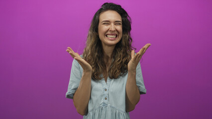 Naklejka premium Hispanic woman raises clenched fists and spreads open palms in a vibrant purple studio scene; excitement triumph celebration.
