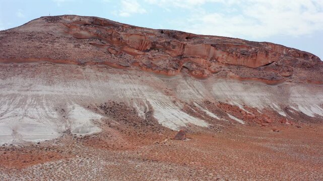 aerial camera moving sideways along layered hill face wide shot in Mangystau Kazakhstan, lateral motion revealing white and red strata bands and surface erosion across dry desert terrain