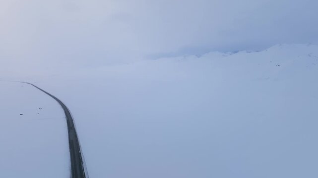 Aerial footage of a lonely paved road cutting through a vast snow-covered plateau at Ala-Bel Pass, Naryn Region, Kyrgyzstan, under overcast winter sky