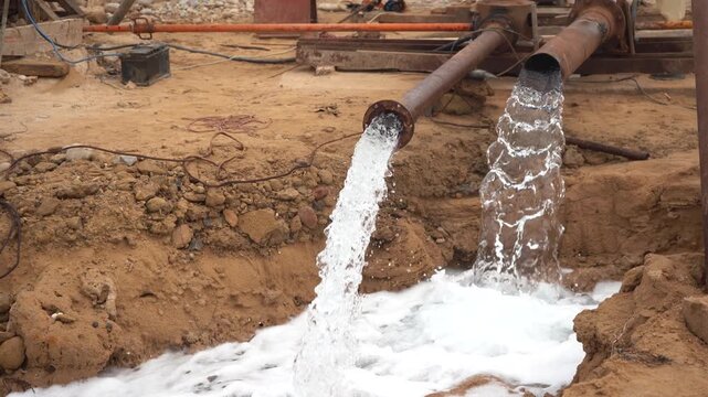 Rusty industrial pipes continuously pump a massive flow of water into a muddy trench. Features live pump engine audio. Ideal for construction dewatering, well drilling, and irrigation Broll with sound