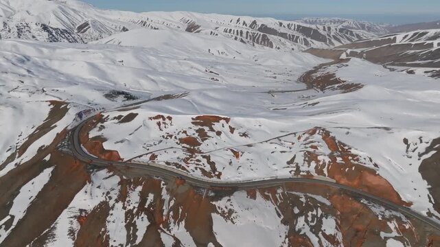 Drone footage of a winding mountain highway crossing Chyyyrchyk Pass, Kyrgyzstan, with snow-covered ridges, red rock slopes, and a vast winter landscape