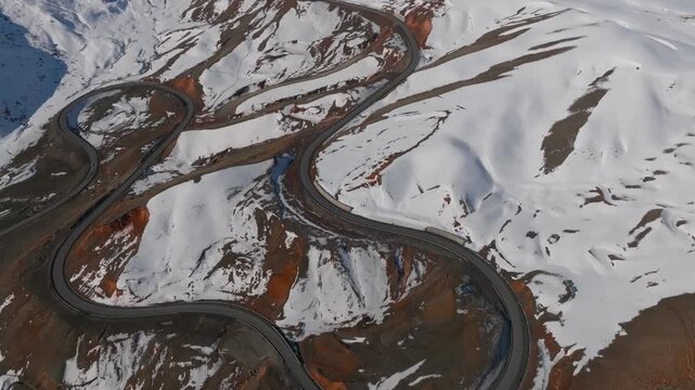 Drone footage of a serpentine mountain highway with sharp hairpin turns across snowy slopes at Chyyyrchyk Pass, Kyrgyzstan, scenic winter travel landscape