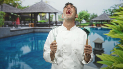 Naklejka premium Man chef holds whisk and ladle with hands, looks up laughing beside a hotel building pool; joyful celebration.
