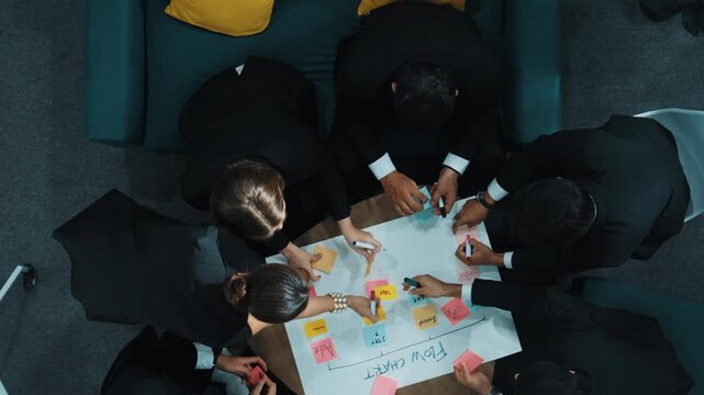 Top down view of business people hands making scrum task board to manage workflow in workplace. Diverse marketing team drawing a line and use colorful stick notes to work on kanban. Directorate.