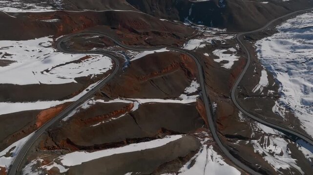 Drone footage of a serpentine asphalt road climbing through rugged highlands with snowfields and barren slopes at Chyyrchyk Pass, Kyrgyzstan in winter light