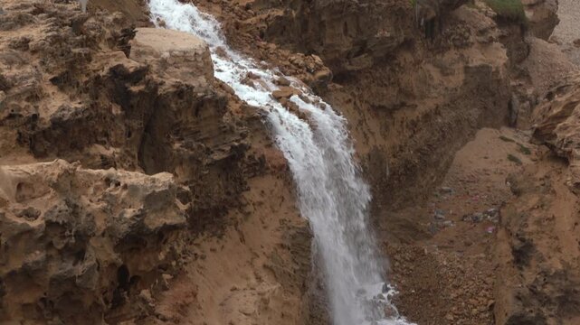 Tilt-down shot of wastewater cascading from a residential settlement over a steep, eroded cliff into rocky, litter-filled ravine. Perfect B-roll for documentaries on poor infrastructure and pollution.