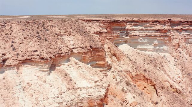 aerial view of Bozzhyra canyon cliffs in Mangystau Kazakhstan showing layered white chalk limestone and red clay strata, ancient marine sediment formations shaped by erosion and wind in arid plateau
