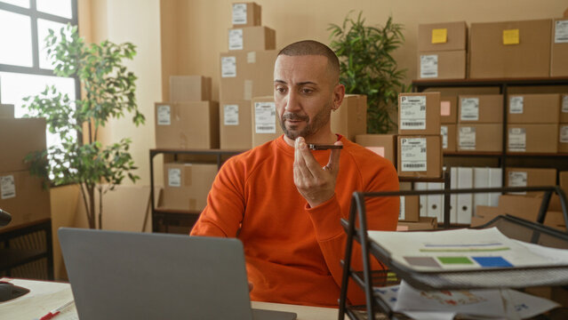 Man holding smartphone to mouth while working on laptop in parcel building; small business determination.