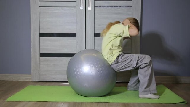 Detailed view of young child performing abdominal crunches on large gray stability ball, promoting physical activity and healthy lifestyle.