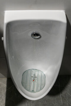 White ceramic urinal in public restroom with plastic splash screen. Clean modern urinal mounted on a grey tiled wall in a commercial bathroom interior.