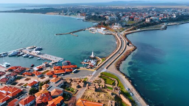 Aerial view of coastal town peninsula with historical ruins. High angle shot of a narrow road connecting an old city to the mainland surrounded by turquoise sea water.