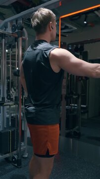 Athletic man trains rear deltoid muscles on cable machine in dark modern gym with orange LED lighting