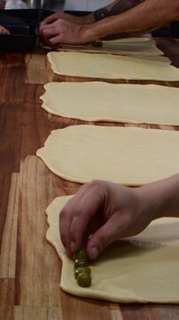 Hands of bakers assembling several pan de jamon rolls on wooden table