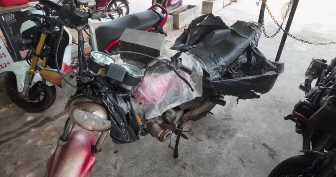 Close up of a weathered red motorcycle outdoors, makeshift protected with tattered plastic bags and a heavy stone block.