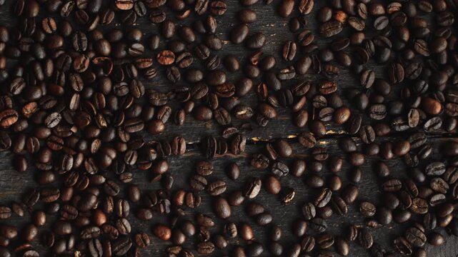 Roasted coffee beans pouring and filling the frame on a dark rustic wooden background, top view