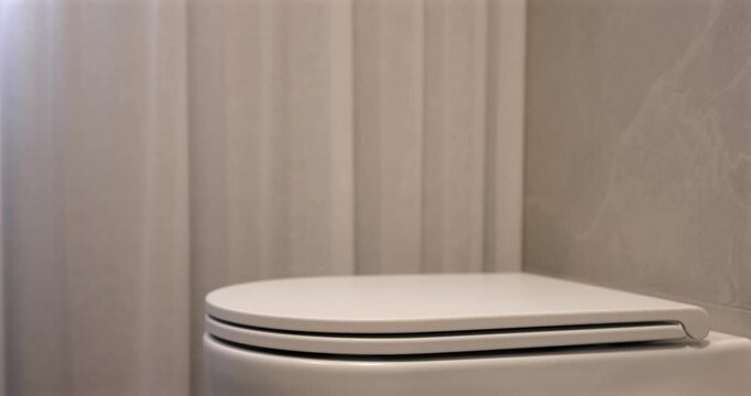 Soft close toilet lid in modern bathroom, static interior video captures white ceramic fixture as seat lowers gently in natural daylight beside sheer curtain creating clean quiet domestic scene