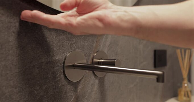 Touchless lighting activation under modern mirror with soft halo glow, static bathroom footage focuses on palm gesture that switches integrated backlight above textured stone and sleek premium sink