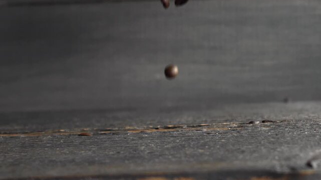 Roasted coffee beans falling and bouncing on dark wooden surface in slow motion forming a pile
