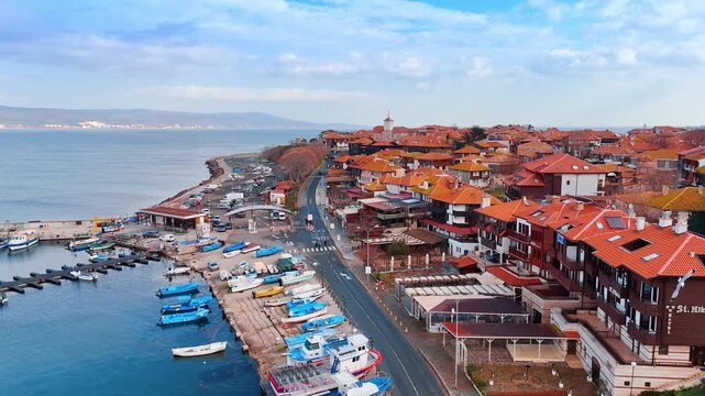 Harbor with blue fishing boats docked at old town. Aerial view of a marina filled with small wooden boats along a paved pier next to traditional buildings.