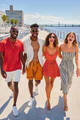 Fototapeta premium Four friends walking along a sunny riverfront boardwalk laughing and enjoying a summer day together