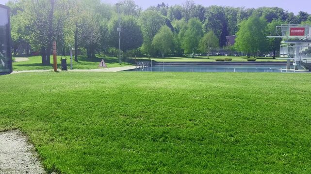 Summer pool season preparation with fresh green lawn irrigation, water sprinklers spraying over grass near outdoor swimming pool, sunny day, landscaping maintenance