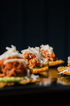 Mini patacones with shredded meat and cabbage slaw on black surface, crispy latin street food appetizer concept