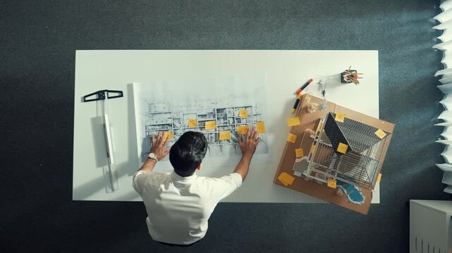 Top down view of architect engineer writing building structure idea on note and stick on blueprint. Aerial view of manager working on notes or taking a notes while open project plan. Alimentation.