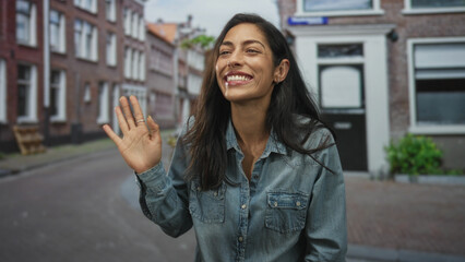 Fototapeta premium Woman smiling and holding hair with hand on a narrow street lined with brick buildings; joy candid moment.