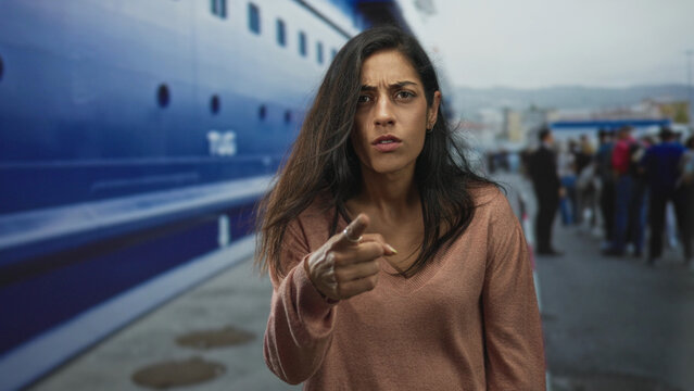 Woman frowning with furrowed brow standing near a ship at port under overcast sky; frustration solitude travel.