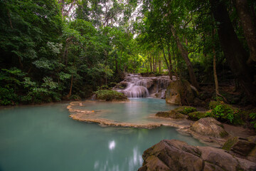 A turquoise waterfall cascades down in layers in the middle of the forest. © Pongsorn