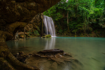 A turquoise waterfall cascades down in layers in the middle of the forest. © Pongsorn