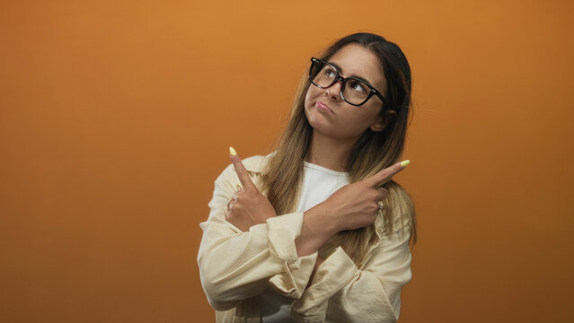 Woman crossing arms and pointing fingers showing yellow nails in studio with orange backdrop; defiance.