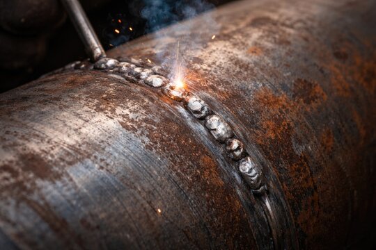 Metal pipe seam welding using tack weld technique showing rust and texture flaws
