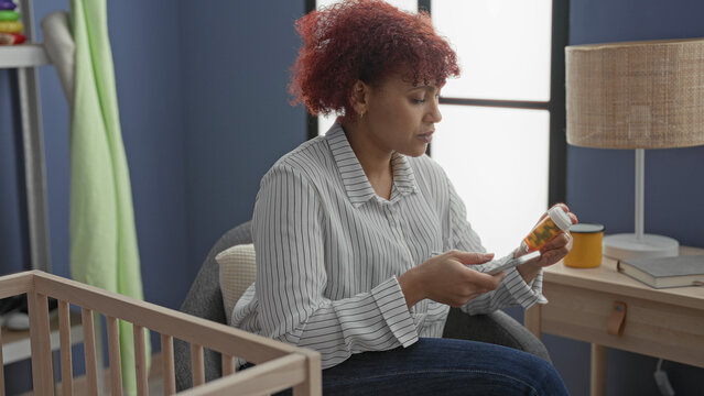 Woman holds pill bottle and smartphone reading label and checking dosage in baby room beside crib; parental concern.
