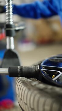 Close-up of automotive tire mounting on alloy wheel using professional tire changer in a service workshop, with hydraulic arm pressing bead as mechanic operates equipment
