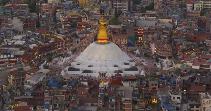 Aerial view of the golden top of Boudhanath Stupa, a UNESCO World Heritage Site in Kathmandu Nepal, centered in a busy square surrounded by crowded streets and dense buildings in fading evening light.