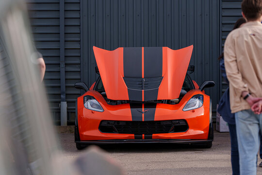 Front view of an orange Chevrolet Corvette C7 Z06 with black racing stripes and open hood, high-performance American sports car on display at an automotive event