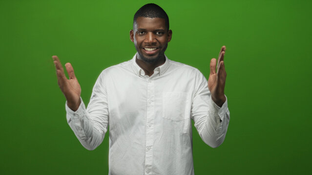 Man claps hands with palms visible, smiling and gesturing toward camera while wearing a white shirt against a green studio backdrop; cheerful.