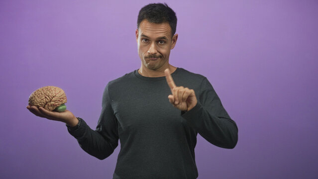 Man holding brain model in left palm while pointing finger with right hand, studio setup with purple backdrop; insightful skepticism.