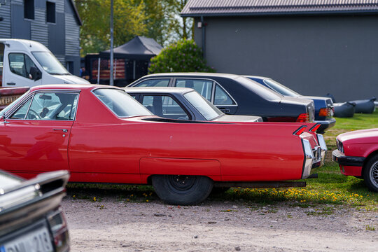 Rear side profile of a red custom Cadillac flower car or pickup conversion featuring iconic tail fins, classic American vintage vehicle parked at an outdoor car meet