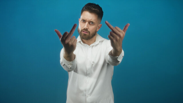Man in white shirt extends hands and shows middle fingers toward camera in studio; defiance provocation.