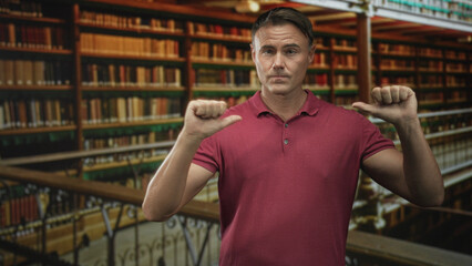 Man in red polo pointing thumbs at his chest amid tall bookshelves and iron balcony rail in a historic library building  confidence identity. © Krakenimages.com