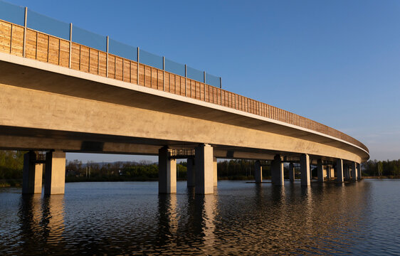  Nowoczesna estakada drogowa nad rzeką o zachodzie słońca, architektura inżynieryjna.